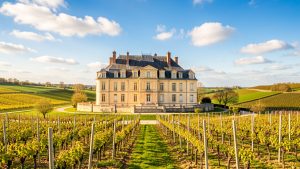 Vue lumineuse du Château de Cassaigne, avec sa façade Renaissance entourée des vignes de Ténarèze sous un ciel bleu de printemps.
