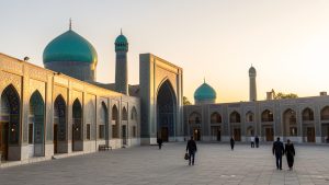 Vue panoramique du Registan à Samarcande au lever du soleil, avec ses coupoles turquoise, sa lumière dorée et quelques voyageurs discrets dans la cour historique.