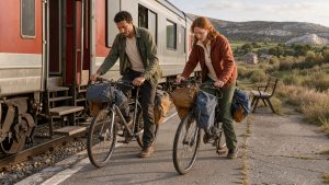 Un homme et une femme descendent d’un train régional avec leurs vélos de randonnée sur le quai d’une gare du Sud-Aveyron, avec des paysages calcaires en arrière-plan.